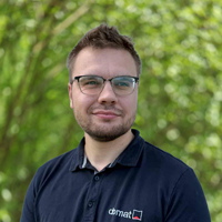 Portrait of a man with short hair and glasses wearing a dark polo shirt, standing outdoors with green trees in the background.