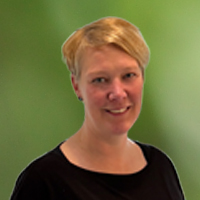 Head-and-shoulders portrait of a smiling woman with short blonde hair wearing a black top, against a green blurred background.