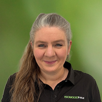 Portrait of a smiling woman with long hair wearing a black polo shirt with a logo, outdoors with a green background.