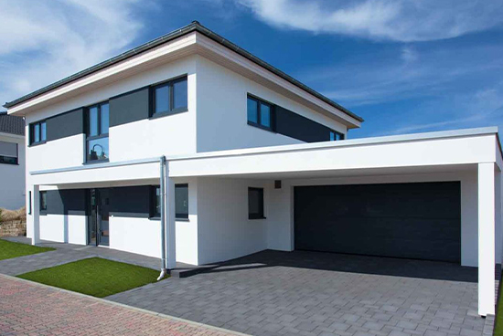 Front view of a modern white two‑story house with black window frames, gray accents, and a large dark two‑car garage door under a covered driveway.