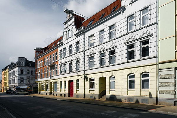 Row of colorful, historic buildings along a quiet street, dominated by a white ornate facade with arched entrances and windows.
