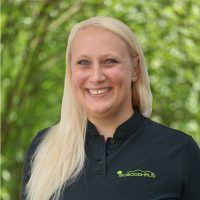 Portrait of a smiling woman with long blonde hair outdoors, wearing a black polo with a Sowoodhaus logo.